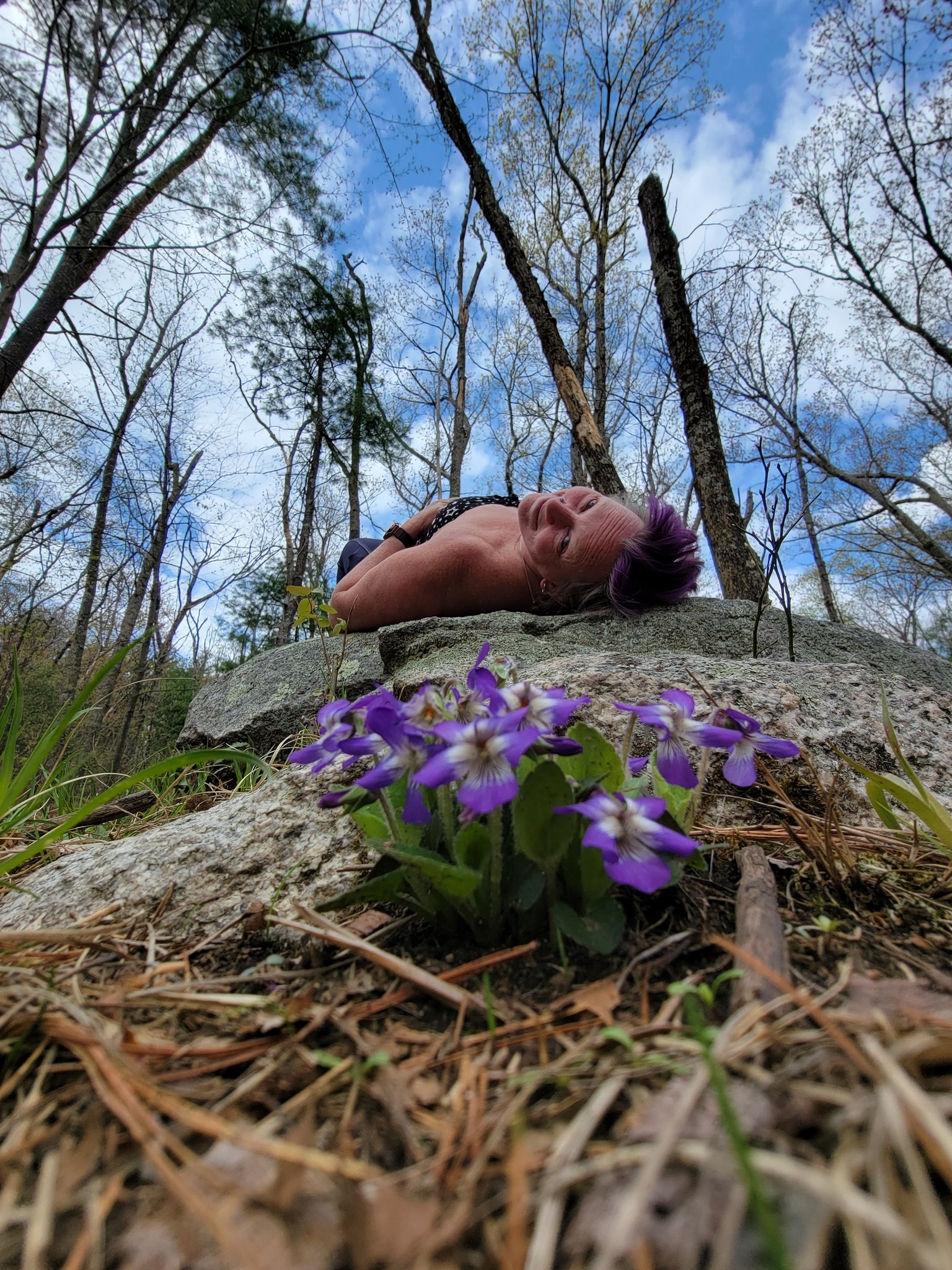 What is a feral woman? Show is an interesting angle of a woman relaxing on a rock with purple flowers in the foreground.